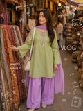 Model walking through a market wearing the viral Zarysh ready-to-wear lawn collection in green and purple, carrying a white handbag.
